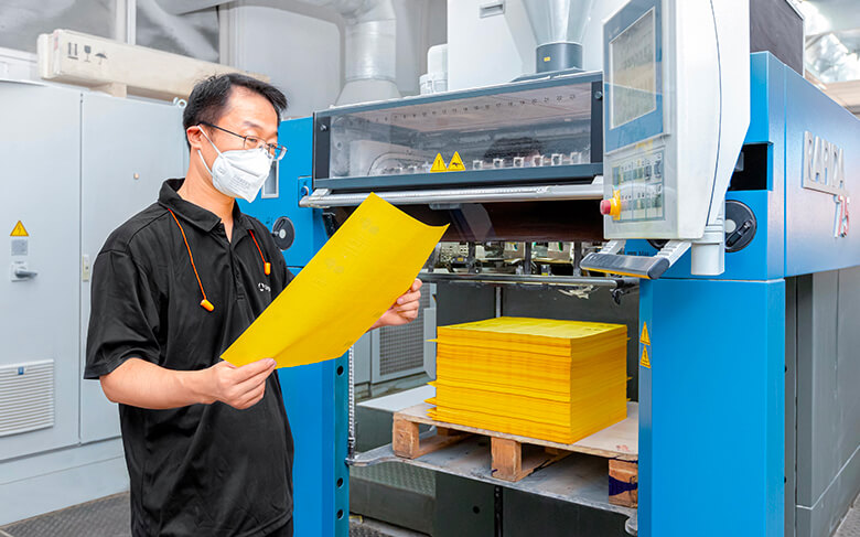 a machine master wearing a mask is standing and checking the printed product in front of the KBA printing machine
